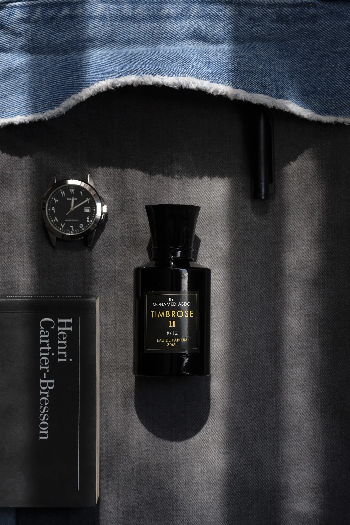 Timbrose II seen from above on grey cloth, with a wristwatch with Arabic numerals, a pen, a book on Henri Cartier-Bresson and the edge of a denim jacket